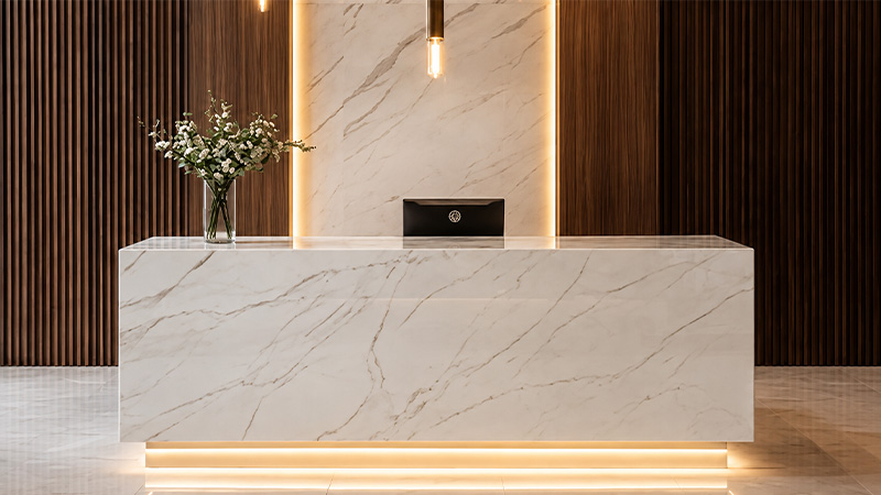 Hotel lobby reception area featuring a high pressure marble-finish laminate desk and dark wood fluted HPL wall panelling.